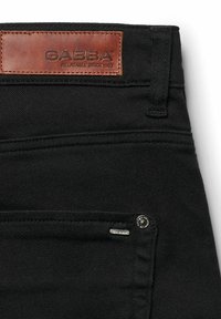 Černá denimová tkanina s koženou etiketou s nápisem "GABBA" vyšitou na pase. Obsahuje detail ze stříbrného kovového materiálu a jemné švy.