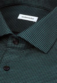 Donkergroen overhemd met patroon en geweven textuur, zwarte knopen en een wit label met "seidensticker" geborduurd op de kraag.