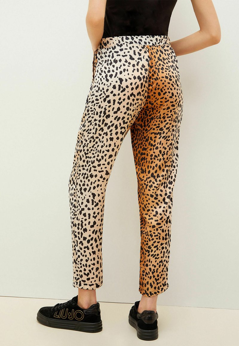 Pantalones de satén con estampado de leopardo en beige y naranja, con un corte ajustado y un diseño a la altura del tobillo, combinados con zapatillas negras.