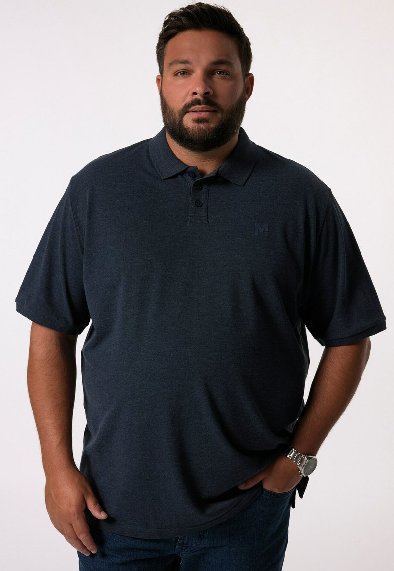 Tmavě modré polo tričko z prodyšného materiálu, s límečkem, plaketou na tři knoflíky a nenápadným logem. Spárováno s tmavými džínami.