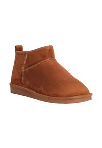 Botas de tobillo de ante marrón con un perfil bajo, punta redondeada y detalles de costura. Textura suave con una suela flexible y una lengüeta en la parte trasera.