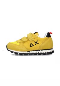 Sneaker giallo in pelle scamosciata con cinturini in Velcro, accenti neri, suola intermedia bianca a zigzag e dettaglio del logo. Presenta una punta arrotondata e suola texturizzata.