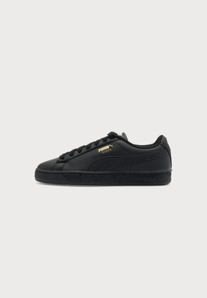Baskets basses Puma Suede noires avec lacets noirs, semelle texturée et logo Puma doré sur le côté.