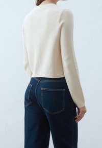 Krämsfärgad stickad tröja med ett strukturerat mönster och ribbad krage, tillsammans med mörkblå högmidjade jeans som har bakfickor.