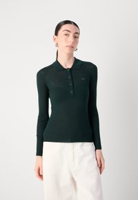 Temno zelena rebrasta majica s longsleeve polo izrezom in gumbnim zapiranjem, s teksturirano tkanino in majhnim logotipom na prsih.