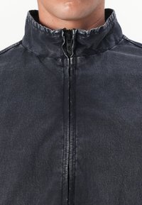 Casaco preto com fecho éclair e gola alta em tecido texturizado. Apresenta um fecho à frente e um design minimalista sem logótipos visíveis.