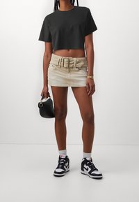 Svart cropped t-shirt, ljusbeige denim minikjol med bredt bälte, svart handväska, vita strumpor och svart-vita högställda sneakers.