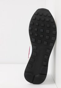 Semelle de chaussure Nike en caoutchouc noir, dotée de chevilles carrées pour une traction optimale. Surface texturée avec détail du logo. Design minimaliste, sans motifs visibles.