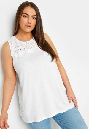 Witte mouwloze top met oogjesdetails bij de halslijn. Zachte, lichtgewicht stof en een ontspannen pasvorm, gecombineerd met blauwe jeans.