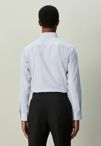 Vaaleansininen ja valkoinen ruutukuosinen pitkähihainen napillinen paita, valmistettu puuvillasta. Ominaisuuksiin kuuluu klassinen kaulus ja istutettu malli, yhdistetty tummiin housuihin.