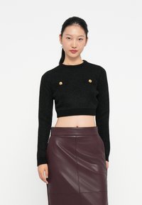 Μαύρος κοντός που ειναι φούτερ με υφή, διαθέτει χρυσά κουμπιά και μακριά μανίκια. Συνδυασμένο με φούστα από ψεύτικο δέρμα σε μπορντό χρώμα.