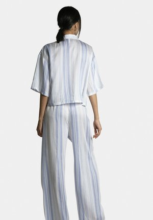 Femme aux cheveux foncés attachés, portant une chemise ample à manches courtes et un pantalon large assorti à rayures verticales bleues et blanches, vue de dos.