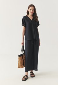 Navy blauwe outfit met een losse, korte mouwen top met V-hals, gecombineerd met wijde pantalon. Gecombineerd met een geweven handtas en zwarte sandalen.