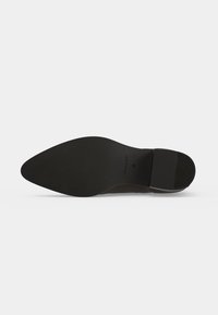 Semelle de chaussure en cuir noir avec bout pointu et talon bas, affichant la marque GANT et la taille 38 sur fond blanc.