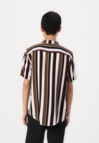 Lyhythihainen paita, jossa on pystysuorat raidat ruskeassa, mustassa, valkoisessa ja punaisessa. Lippa-kaulus, rento leikkaus ja sivuviillot helmassa.