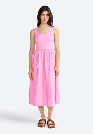 Pink dress with a ribbed bodice and a flowing skirt. Features side pockets, mid-calf length, and is paired with brown sandals.