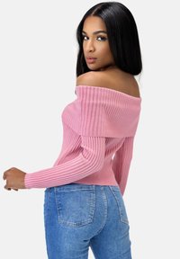 Rosa, schulterfreie, gerippte Pullover mit langen Ärmeln, taillierter Passform, strukturierter Stoff, kombiniert mit blauen Jeans.