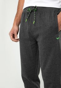 Graue Sweatpants mit einem Kordelzugbund, die schwarze und neongrüne Akzente aufweisen. Hergestellt aus weichem Stoff, mit seitlichen Taschen und einer lockeren Passform.