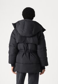 Black puffer jacket with a cinched waist, large hood, and quilted pattern. Features elastic cuffs and a relaxed, oversized fit.