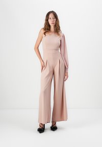 Vaaleanpunainen jumpsuit, jossa on yksi pitkä hiha ja istuva vartalo. Siinä on leveät lahkeet ja poimutuksia, ja se on valmistettu sileästä, teksturoidusta kankaasta.