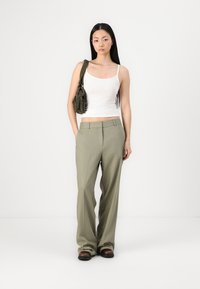 Pantalon vert ajusté avec une coupe droite, associé à un débardeur blanc. Un petit sac olive avec des franges est porté à l'épaule.
