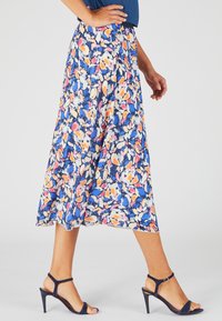 Falda midi floral de tejido ligero, con una mezcla de patrones azules, naranjas y rosas, con una textura suave y una forma acampanada.