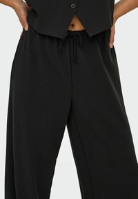 Pantalons larges noirs en tissu doux et léger. Présentent une taille élastique avec un cordon de serrage pour un ajustement réglable.