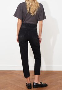 Vaqueros negros de talle alto con un ajuste ceñido y piernas rectas, que cuentan con dos bolsillos traseros y un tejido texturizado. Diseño minimalista.