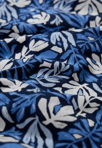 Granatowa tkanina z botanicznym wzorem, na którym znajdują się niebieskie i białe liście. Materiał jest miękki i teksturowany, ukazujący niezwykle szczegółowe wzory liści.