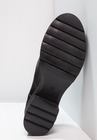 Svart skosula med breda horisontella spår, storlek 37 märkt, placerad upprätt mot vit bakgrund.