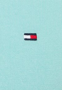 Maglione lavorato a maglia di un tenue verde menta con un piccolo logo ricamato che presenta strisce rosse, bianche e blu sul petto.