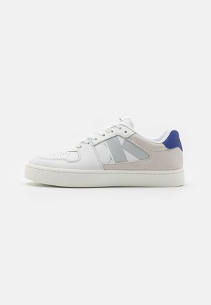 Sneakers bianchi con tomaia in pelle liscia e accento in tessuto grigio. Presentano un tallone blu e un logo decorato sul lato. Suola in gomma.