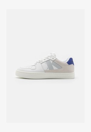 Sneakers bianchi con tomaia in pelle liscia e accento in tessuto grigio. Presentano un tallone blu e un logo decorato sul lato. Suola in gomma.