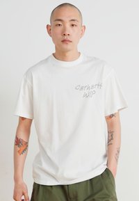 Balta medvilnės marškinėliai trumpomis rankovėmis, su subtiliu pilku siuvinėtu "Carhartt WIP" logotipu kairėje krūtinės pusėje. Minimalistinis dizainas.
