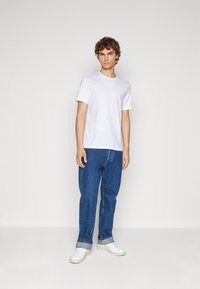 White cotton t-shirt with a crew neckline paired with relaxed-fit blue denim jeans. Features rolled cuffs and white sneakers.