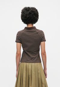 Polo rayé marron à manches courtes, avec un col à revers et une texture côtelée, associé à une jupe plissée vert olive.