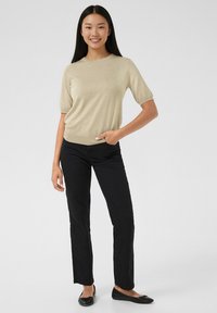 Beige kortærmet sweater med rund halsudskæring, sat sammen med sorte tætsiddende bukser og sorte balletsko. Glat tekstur, minimalistisk design.