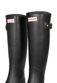 Mustat kumiset sadetossut kiiltävällä pinnalla, joissa on teksturoitu yläreuna, säädettävät hihnat sekä punavalkoinen "HUNTER"-brändäys.