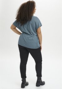 Blauw gemusterde top met een losse pasvorm, korte mouwen, gecombineerd met zwarte skinny jeans en zwarte enkellaarsjes. Gestructureerd patroon op de stof.