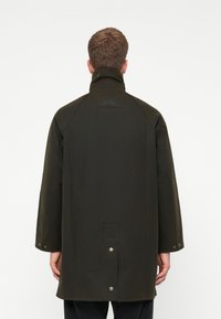Donkergroen waterdichte jas met een hoge kraag, lange mouwen en drukknoopaccenten aan de achterkant. Gladde, matte textuur, modern ontwerp.