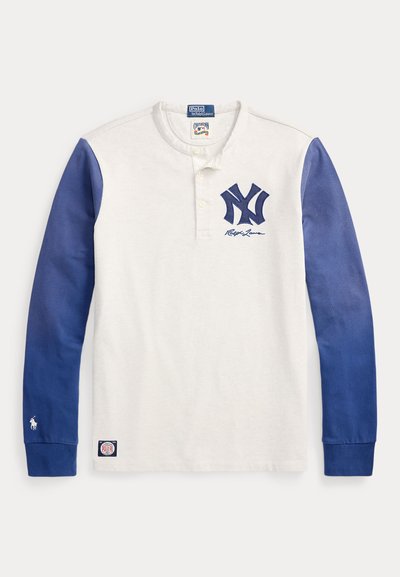 Fehér hosszú ujjú Henley ing kék ujjakkal, tengerészkék "NY" logóval, valamint Polo Ralph Lauren márkajelzéssel a mellkason és a mandzsettákon.