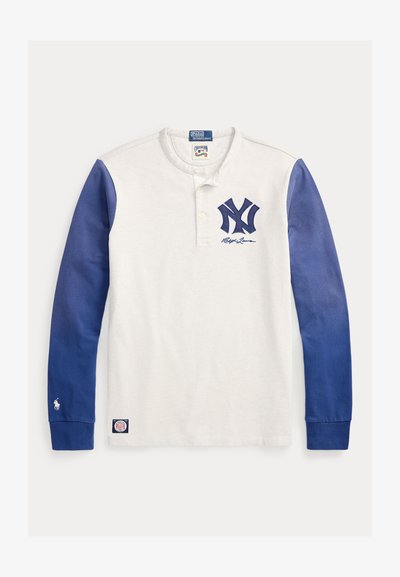 Fehér hosszú ujjú Henley ing kék ujjakkal, tengerészkék "NY" logóval, valamint Polo Ralph Lauren márkajelzéssel a mellkason és a mandzsettákon.