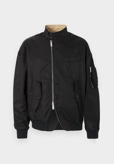 Blouson aviateur noir avec fermeture éclair frontale et fermeture par boutons, deux poches à boutons, poche zippée sur la manche et doublure de col intérieure beige.
