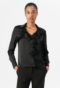 Fekete szatén blúz fodros elülső résszel, hosszú ujjakkal és berepedt gallérral. Sima textúra, testhezálló fazon és gombos záródás elöl.