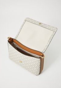 Geantă albă din pânză cu un model subtil de monogramă, accente din piele bej, finisată cu accesorii aurii și un închizător tip snap. Interiorul are o căptușeală bej.