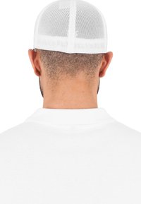 Witte mesh pet met een gladde textuur, voorzien van een gestructureerde achterkant en een verstelbare band. Het ontwerp heeft ventilatiegaten voor ademend vermogen.