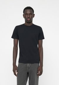 Tricou negru cu mânecă scurtă, din bumbac, cu decolteu rotund, asortat cu blugi gri din denim. Croială fit structurat și textură netedă.