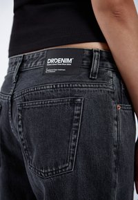 Black denim jeans featuring a straight fit, visible stitching, back pockets, and a branded label. The texture appears slightly faded.