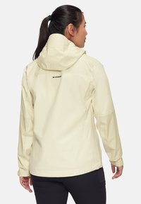 Hellgelbe wasserdichte Jacke mit Kapuze, Netzpaneelen, sichtbaren Nähten und einem Logo auf dem Rücken. Verfügt über verstellbare Manschetten und Taschen.
