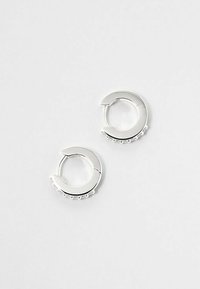 Orecchini a cerchio in argento con forma circolare e finitura lucida, caratterizzati da una fila di piccole pietre trasparenti lungo il bordo.